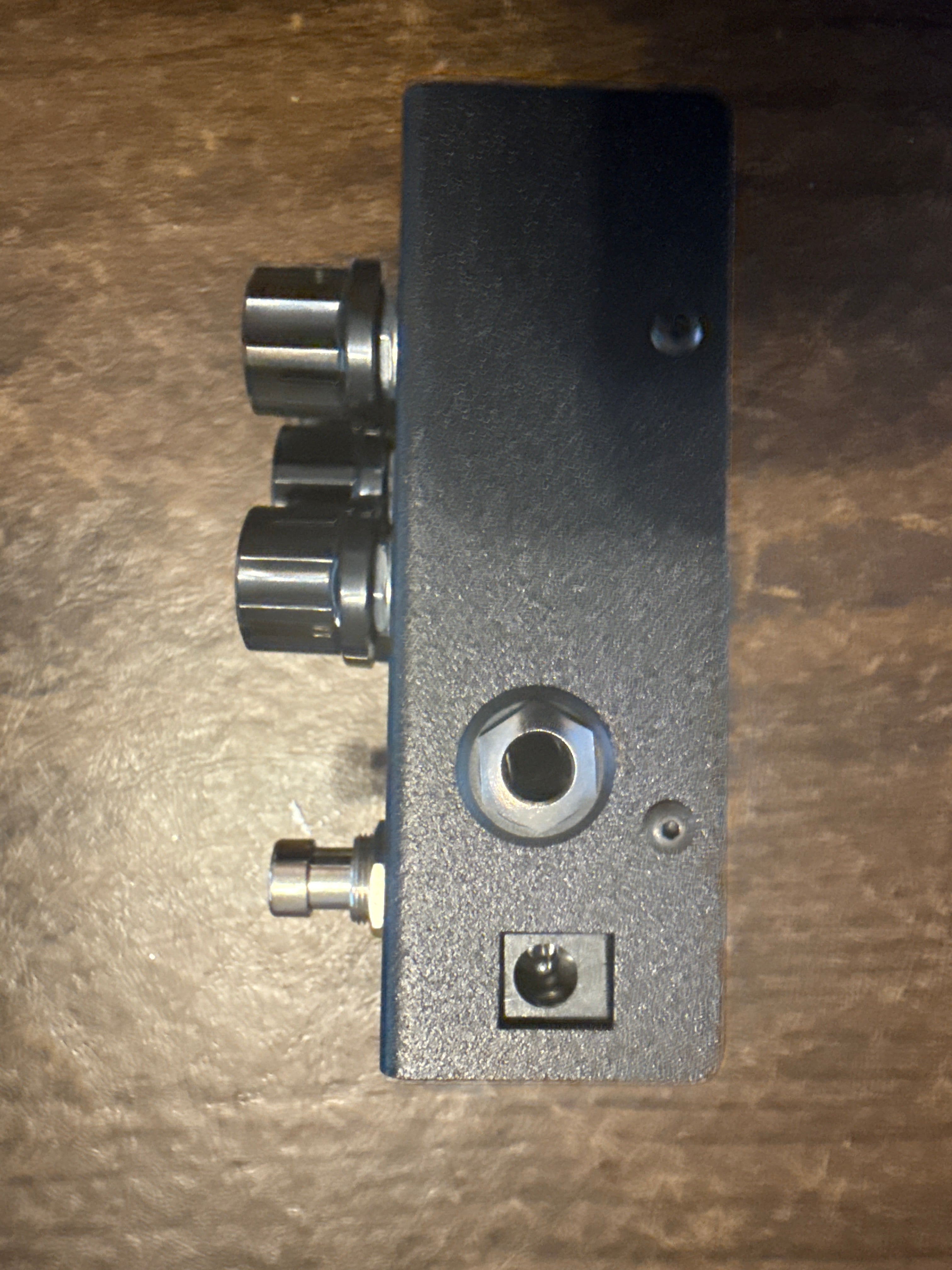 Guitar effects pedal with various knobs and ports on a wooden surface