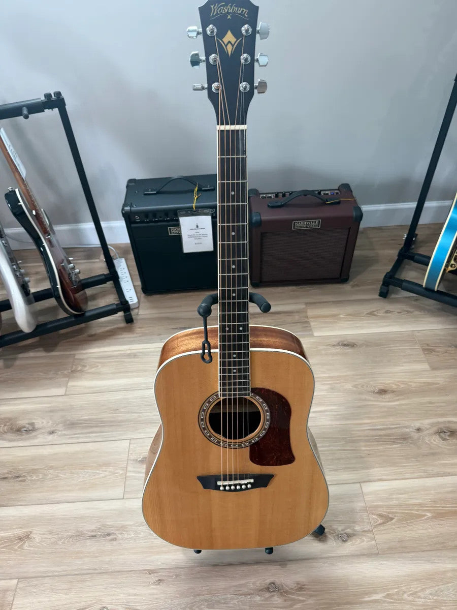 Used Washburn HD10S Heritage acoustic guitar with a natural wood finish and classic shape displayed on a soft surface.
